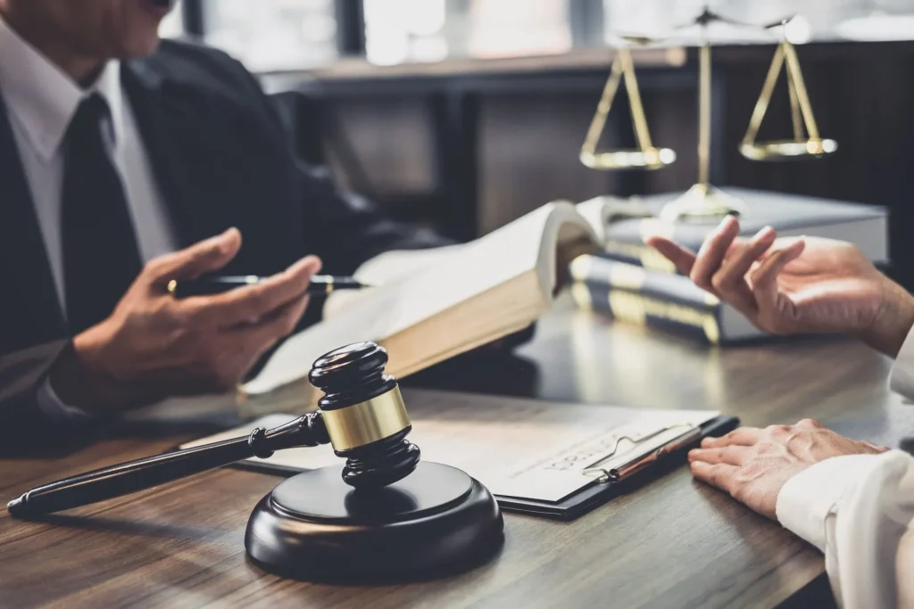 A criminal defense attorney is consulting with a client over legal documents, with a judge’s gavel, law books, and scales of justice symbolizing expert legal guidance and the protection of clients’ rights.