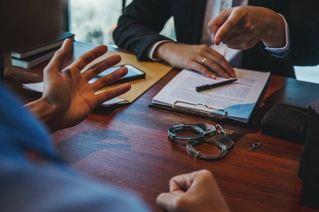 Criminal Defense Attorney discussing a client’s case and reviewing legal documents beside handcuffs, helping protect the client’s rights and build a strong legal defense.